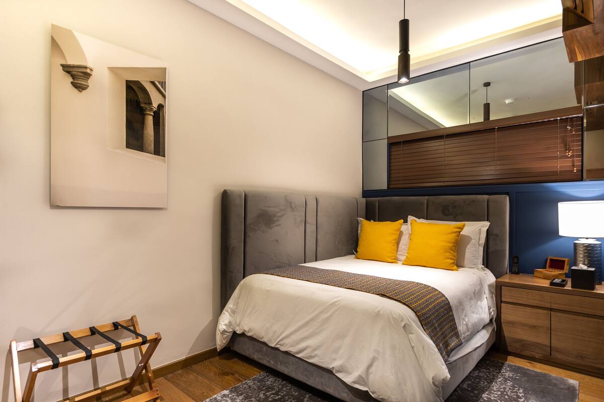 Quarto moderno com cama, mesa de cabeceira e espelho.