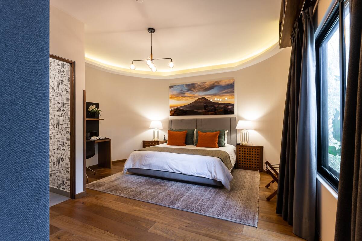 Quarto moderno com uma cama grande, um quadro de montanha e vista do exterior pela janela.
