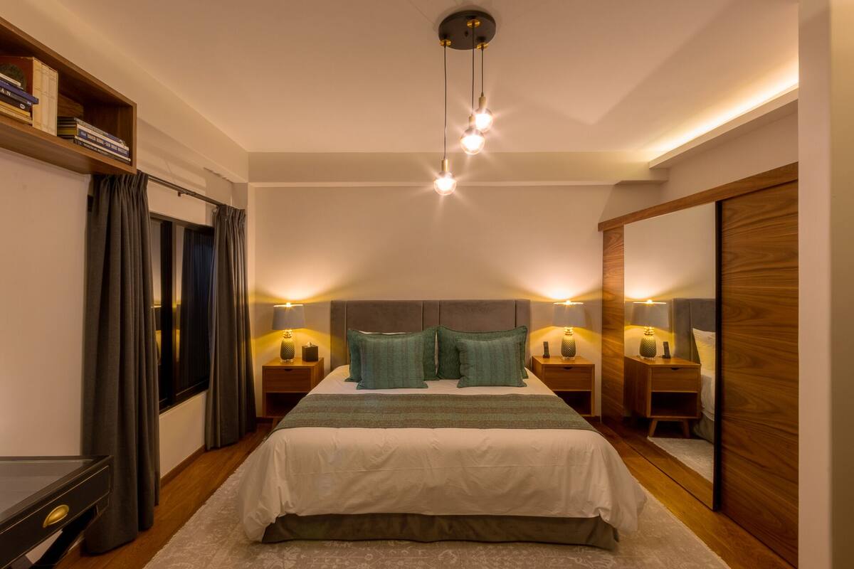 Quarto com uma cama grande, duas mesas de cabeceira com luminárias, um espelho, um guarda-roupa e uma estante.