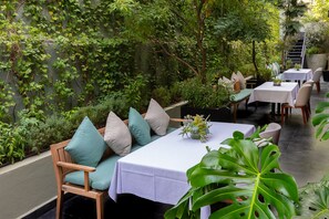 An outdoor dining area with wooden furniture, white tablecloths, and lush greenery.