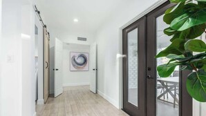 Un couloir doté d’un plancher en bois, d’une porte à cadre sombre et d’une grande plante verte.