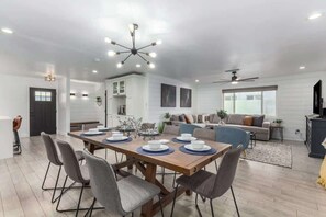 A modern dining area with a wooden table set for six, surrounded by grey upholstered chairs. - Crown Azul | Dual Primarys | 3 Showers | Hottub (Scottsdale)