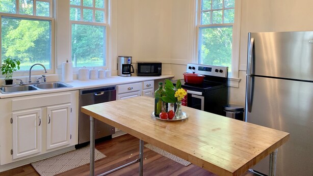 A modern kitchen with white cabinets, a wooden countertop, a stainless steel refrigerator, and large windows offering a view of greenery. - Spacious Home and Private Getaway (Fayette)