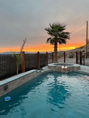 A swimming pool with a hot tub, surrounded by a wooden fence, with a sunset view. - Secluded Oasis, heated pool and spa, RV hook-ups (Bullhead City)
