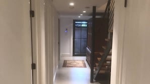 Ein Flur mit weißen Wänden, gefliestem Boden und einer Treppe mit Holzstufen und einem schwarzen Geländer.