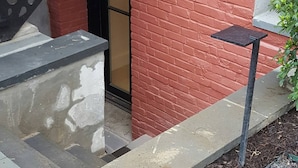 Eine Fassade aus roten Ziegelsteinen mit einer schwarzen Metalltreppe, einem kleinen Tisch im Freien und einem Laternen.