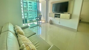 A modern living room with a sofa, a flat-screen TV mounted on the wall, and a sliding glass door leading to an outdoor balcony. - Apartamento Vista al Mar (Cartagena)