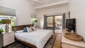 Un dormitorio con cama, mesita de noche, lámpara, televisor y vistas al exterior.