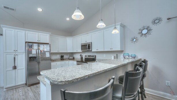 Una cocina moderna con armarios blancos, encimera de granito, electrodomésticos de acero inoxidable e iluminación colgante.