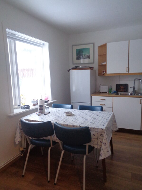 A dining area with a table set for four, a refrigerator, a sink, and a window with curtains. - A cozy artistapartement on ground floor in downtown Siglufjörður, (Siglufjörður)