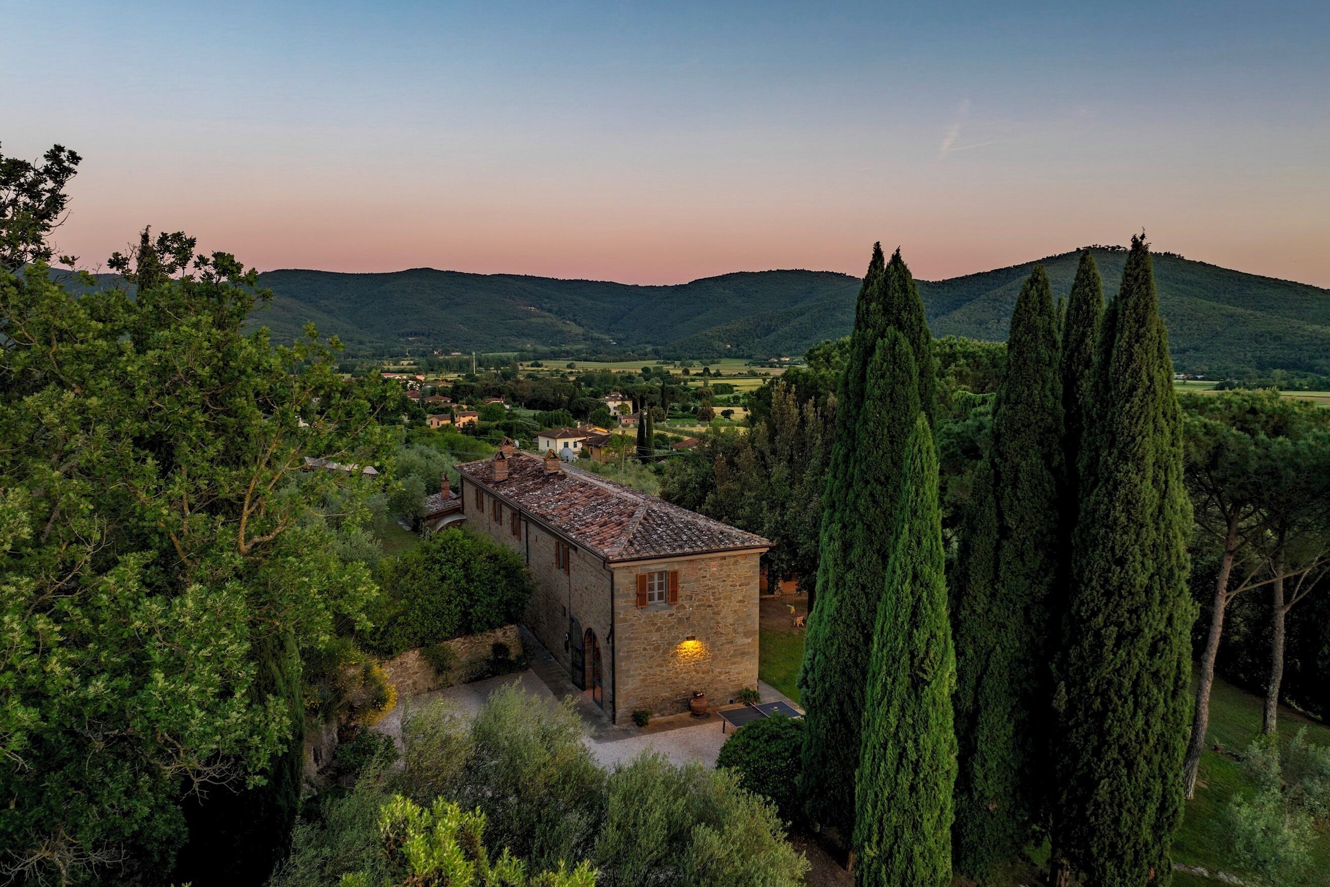 A stone building with a tiled roof surrounded by greenery and hills.