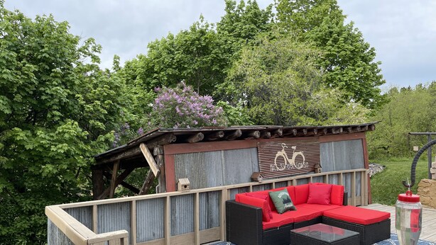 Une terrasse en bois avec un canapé rouge et une table basse en verre, le tout entouré d’un tapis bleu à motifs.