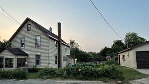 Une maison à deux étages avec un garage, entourée de verdure et sous un ciel dégagé.