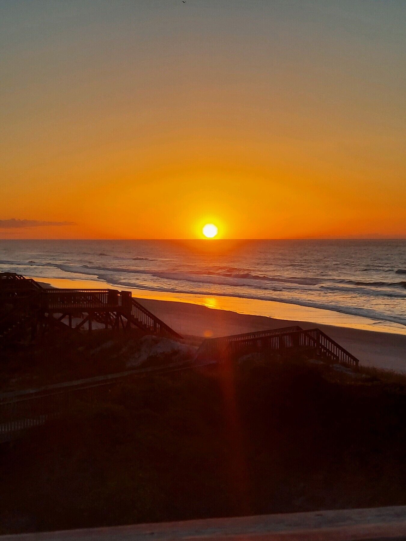 Un atardecer sobre el océano con un muelle de madera que se adentra en el agua.