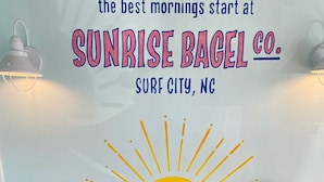 Un mur orné d’un motif représentant un soleil et d’une inscription publicitaire pour Sunrise Bagel Co., situé à Surf City, en Caroline du Nord.