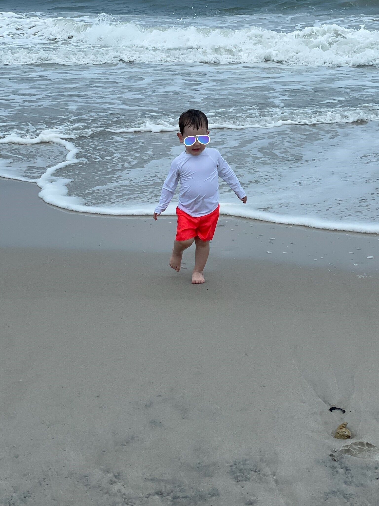 A child walking on a sandy beach with waves in the background.