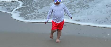 A child walking on a sandy beach with waves in the background.