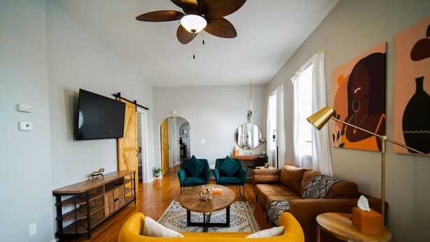 A modern living room with a yellow sofa, a wooden coffee table, and a TV mounted on the wall. - Cozy 3Bed Home w/ Firepit By Zoo, Downtown & I/80❤ (Omaha)
