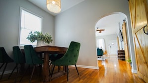 A dining area with a wooden table and green chairs, a potted plant, and a ceiling fan. - Cozy 3Bed Home w/ Firepit By Zoo, Downtown & I/80❤ (Omaha)