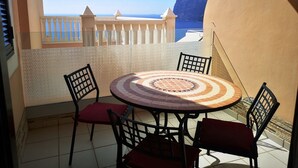 A round table with chairs on a balcony with a view of the sea.