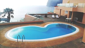 A pool area with a view of the sea, lounge chairs, and a staircase leading to an upper deck.