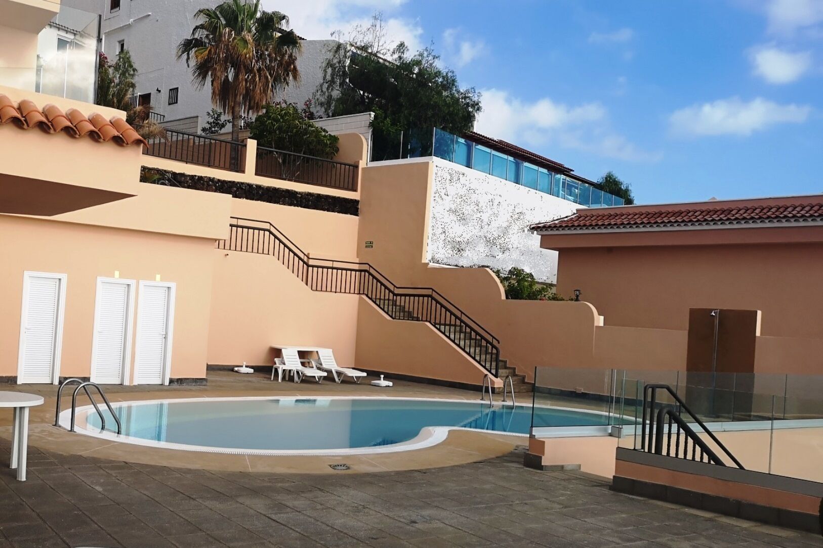 A swimming pool with a glass balustrade, a staircase, and lounge chairs.