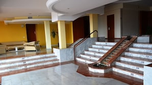 A spacious lobby with marble flooring, a central staircase, and a seating area.