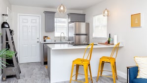 Une cuisine moderne avec des meubles gris, un réfrigérateur en acier inoxydable et un îlot central blanc agrémenté de deux chaises jaunes.