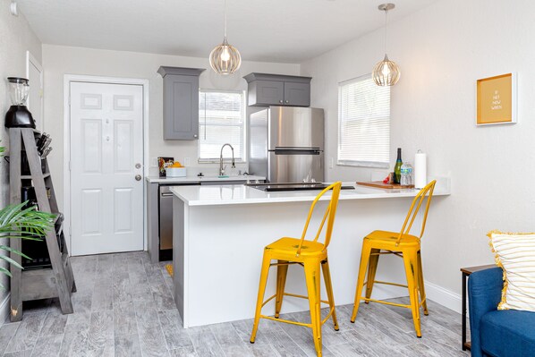 A modern kitchen with grey cabinets, a stainless steel refrigerator, and a white island with two yellow chairs. - Walk to dwnt/7min to beach/king bed/free parking (New Port Richey)