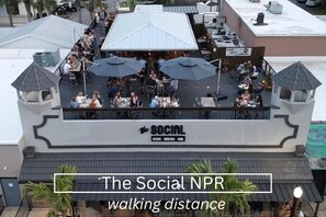 Un espace extérieur aménagé pour les repas au restaurant The Social NPR, avec des parasols et des tables.