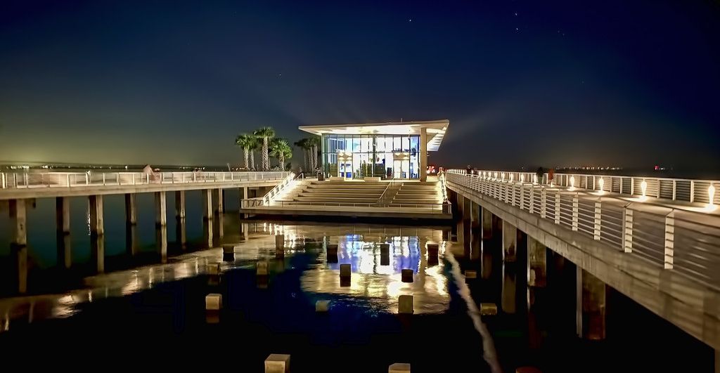Ein Hotel am Wasserufer mit einem Spiegelbecken, einem überdachten Gang und einem Gebäude mit großen Fenstern.