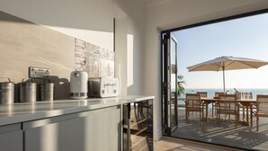 Une cuisine moderne, dotée d’appareils électroménagers en acier inoxydable et offrant une vue sur l’océan grâce à une porte ouverte.
