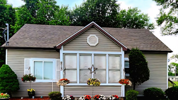 Una casa a un piano con tetto a due falde, un portico con decorazione a stella e il numero '213' sulla parete.