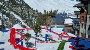 Une station de ski avec un toboggan aquatique gonflable rouge, un paysage montagneux en toile de fond et un bâtiment doté de balcons.