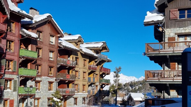 Une station de montagne enneigée, avec des bâtiments à plusieurs étages dotés de balcons et d’une façade en bois.
