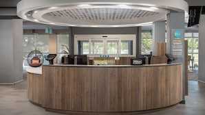 Un mostrador de recepción moderno con terminación de madera, una pantalla digital y un cartel que indica Hilton Trident.