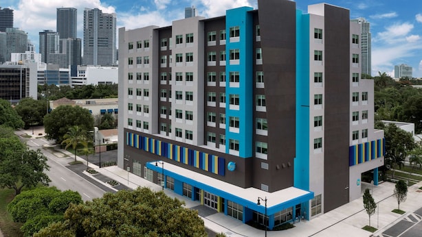 Un hotel de varios pisos con un diseño moderno, que destaca por su fachada azul grisácea, grandes ventanales y techo plano.