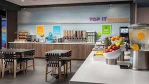 Un área de desayuno con una barra que exhibe diferentes alimentos y un letrero que dice "TOP IT BREAKFAST".