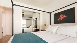 Une chambre moderne avec un grand lit, un plaid turquoise, un panneau lumineux néon sur lequel on peut lire « Los Angeles », et un miroir qui reflète la pièce.