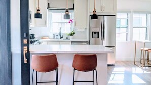 Une cuisine moderne avec des meubles blancs, des appareils en acier inoxydable et des luminaires suspendus.