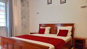 A wooden bed with red and white bedding, a nightstand, and a small wooden cabinet. - Lovely 2-bed Apartment in Kribi-douala (Kribi)
