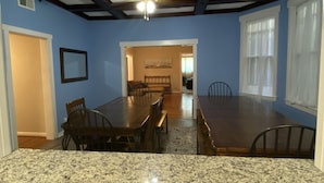 A dining room with a granite countertop, dark wooden table, and chairs. There is a ceiling fan and a window with curtains. - 12-Bedroom Home with Private Pool & Large Yard, About Half Mile to Beach (Galveston)