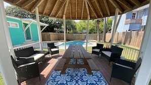 A covered deck with a pool, outdoor furniture, and a view of a house. - 12-Bedroom Home with Private Pool & Large Yard, About Half Mile to Beach (Galveston)