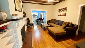 A living room with a fireplace, wooden flooring, a sofa, and a ceiling fan. - 12-Bedroom Home with Private Pool & Large Yard, About Half Mile to Beach (Galveston)