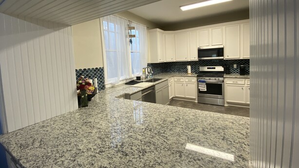 A kitchen with white cabinets, granite countertops, a stainless steel oven, and a microwave. - 12-Bedroom Home with Private Pool & Large Yard, About Half Mile to Beach (Galveston)