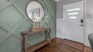 A room with a wooden console table, a round mirror, and a white door with a window. - Hot Tub | Great Location | King Beds | Grill & Patio (Lexington)