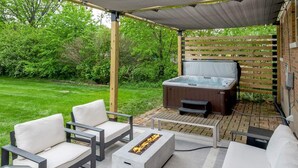 An outdoor patio with a hot tub, seating area, and a pergola with string lights. - Hot Tub | Great Location | King Beds | Grill & Patio (Lexington)