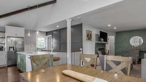A modern kitchen with a dining area, wooden chairs, and a fireplace. - Hot Tub | Great Location | King Beds | Grill & Patio (Lexington)