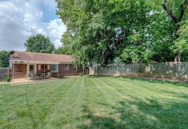 A backyard with a patio, a brick house, and a wooden fence.