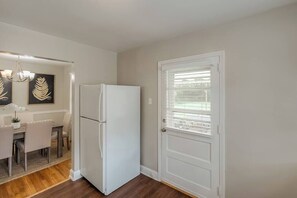 Una cocina con refrigerador, un comedor con mesa y sillas, y una puerta con ventana.